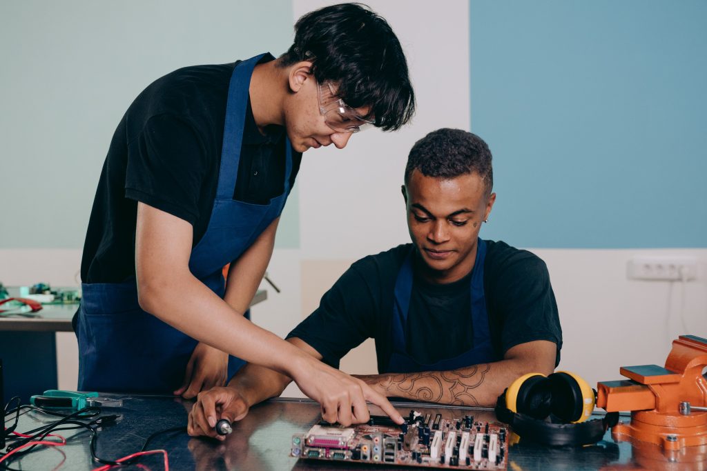 Two young engineers working with electronics in a workshop setting.