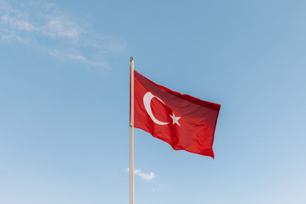 Turkish national flag waving on flagpole against a bright blue sky, symbolizing pride and identity.